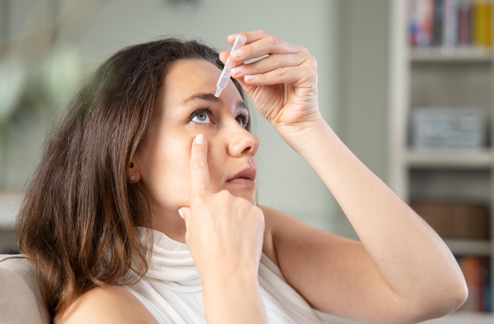 A woman applying eye drops on her right eye to alleviate eye dryness.