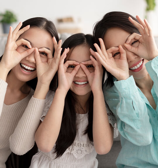 Three girls playfully create glasses with their fingers, giggling as they pose with their makeshift frames.
