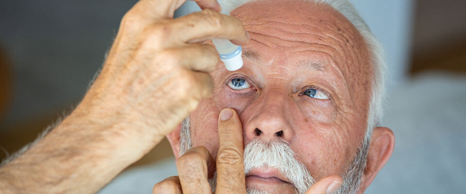 An elderly man administering eye drops