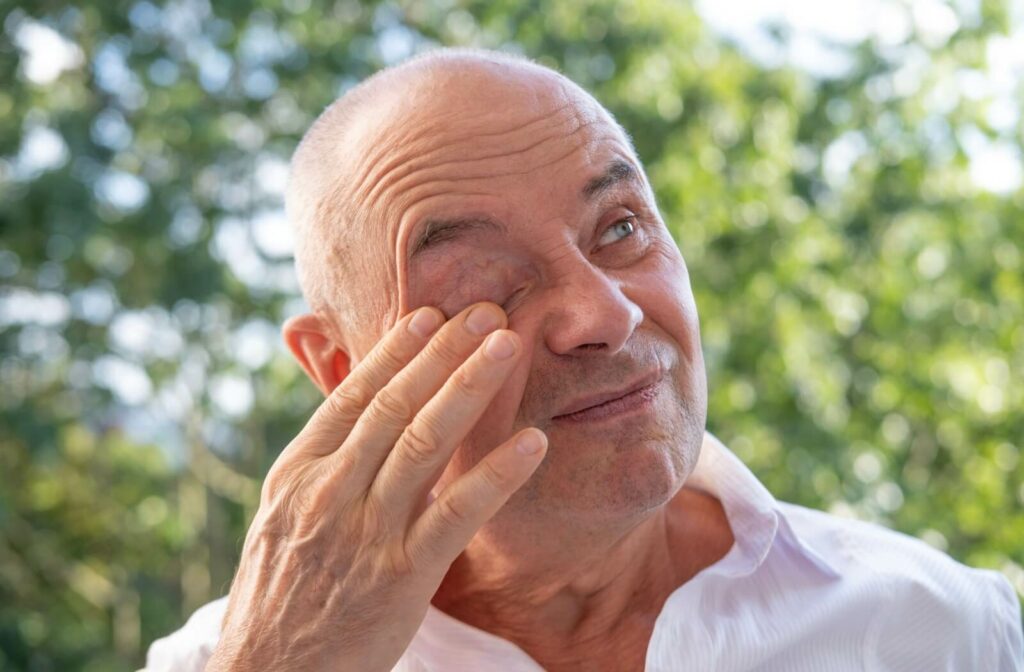 An older man rubbing his left eye due to discomfort caused by an eye condition.