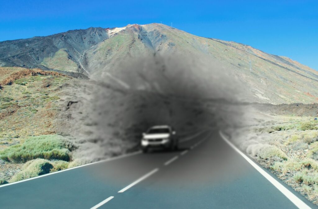 A car drives down a highway in the mountains. The centre is blurry and lacks colour to mimic macular degeneration symptoms