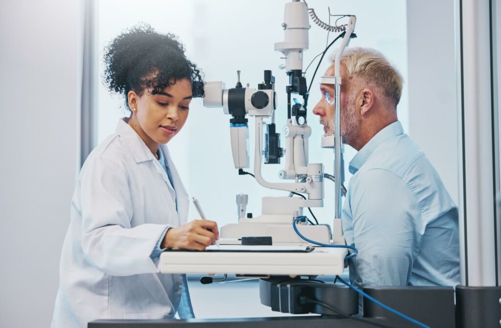 An optometrist takes notes while conducting an eye exam on a patient in a well-lit exam room