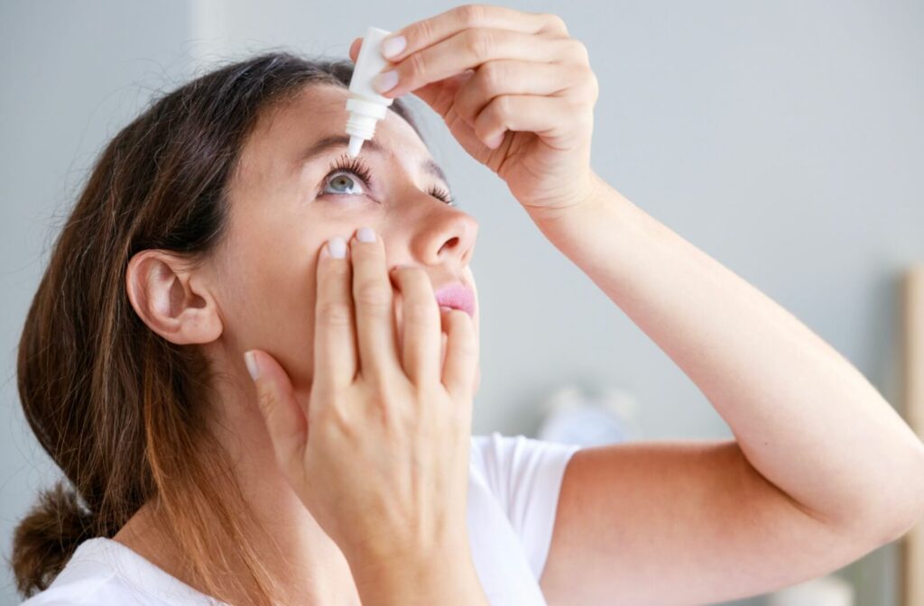 A woman carefully applying eye drops to her right eye to find relief from her dry eyes.