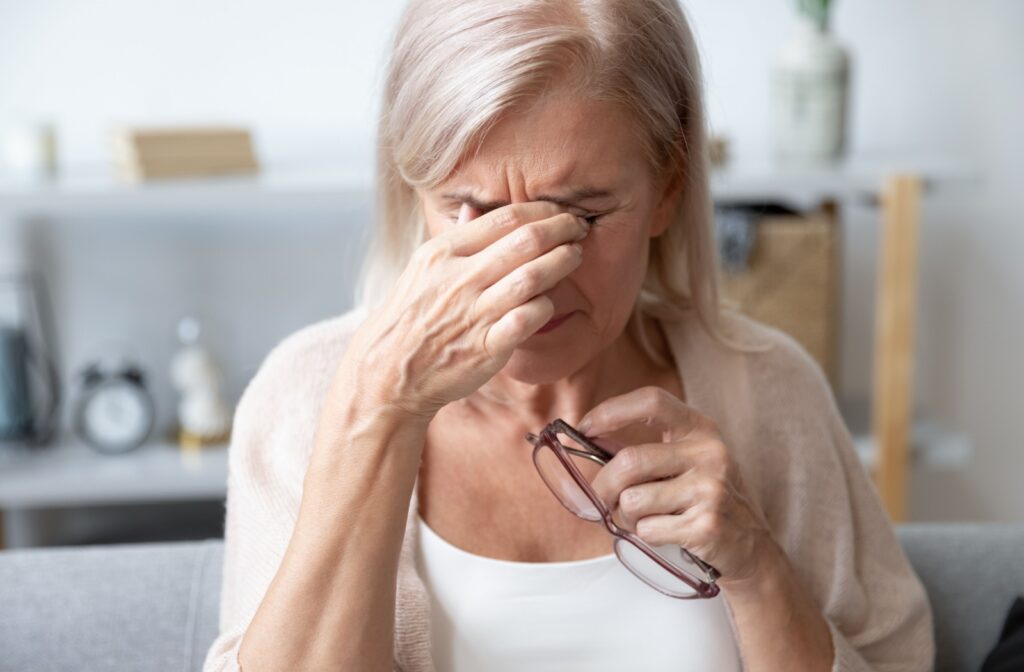 Elderly woman rubbing her eyes while holding her glasses showing symptoms of cataracts like eye discomfort and blurry vision