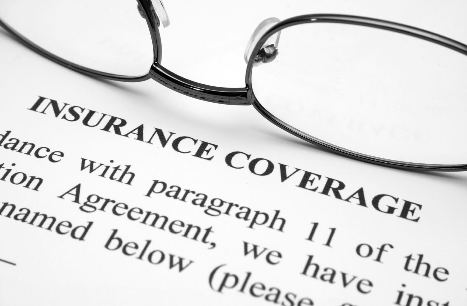 A close-up of eyeglasses resting on a printed insurance coverage document.