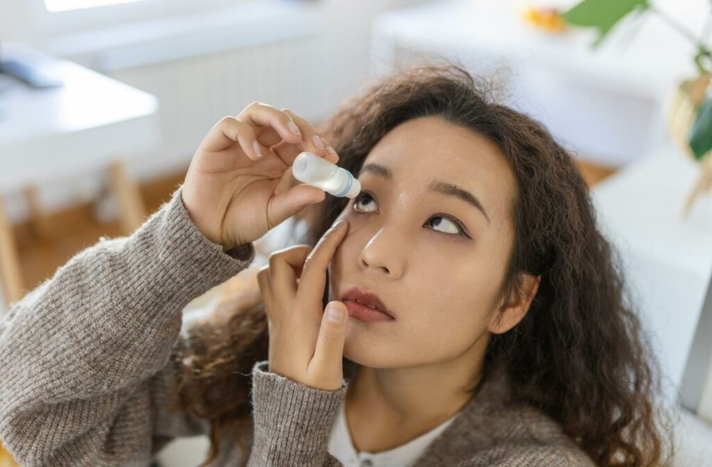 A person applying eye drops while looking upward indoors.