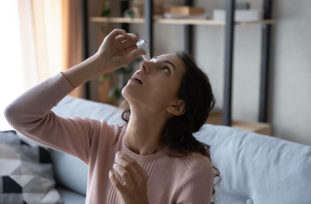 A person using eye drops while sitting on a couch.