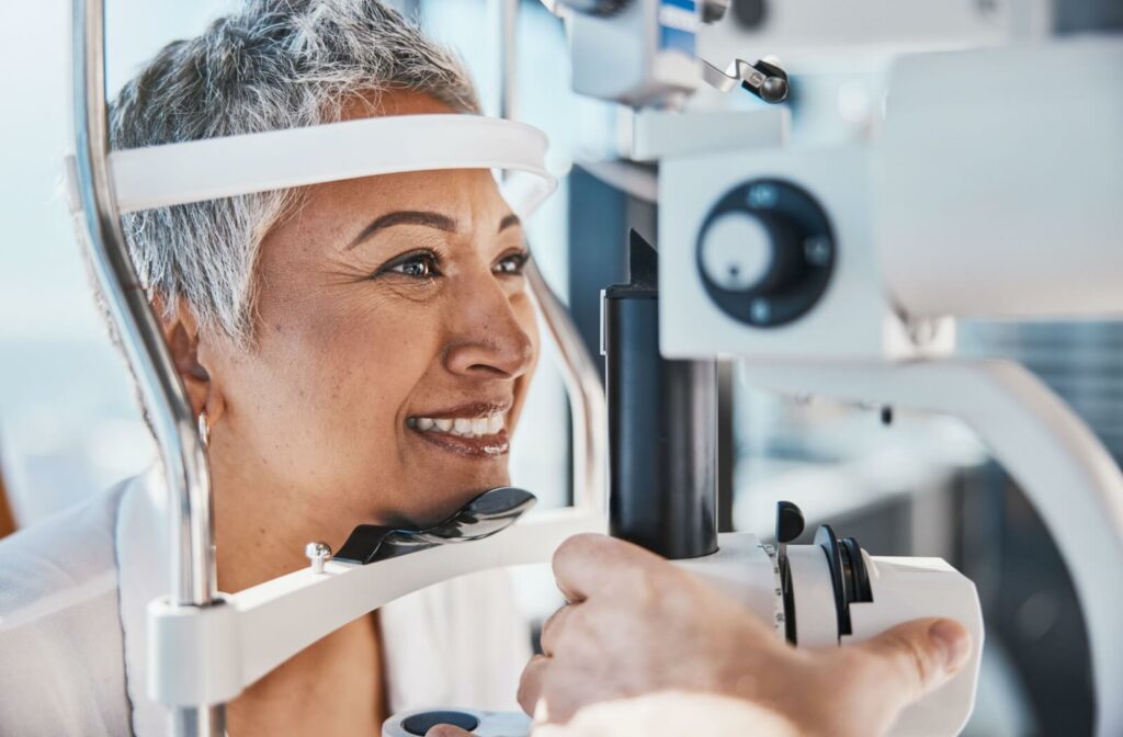Smiling older person receiving an eye exam by resting their chin on optometry equipment.