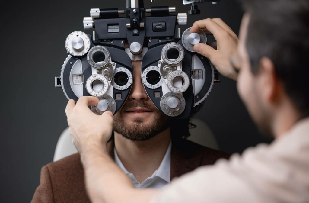 An eye care professional adjusting a phoropter during a vision test for a patient sitting behind the device.